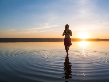Gün batımında sahilde siluet yoga kadınla.