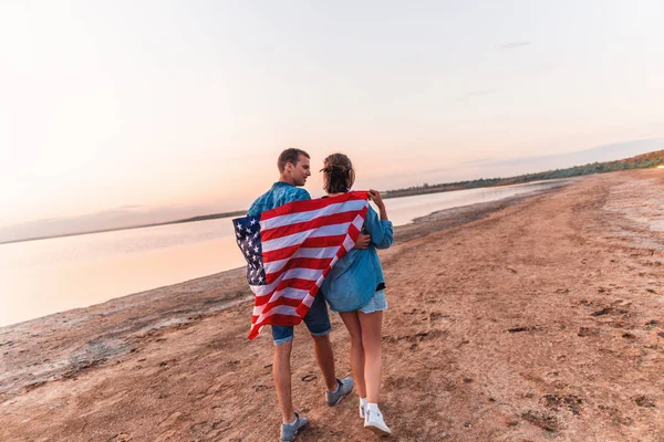 Pareja americana cubierta de bandera americana caminando en la playa — Foto de Stock