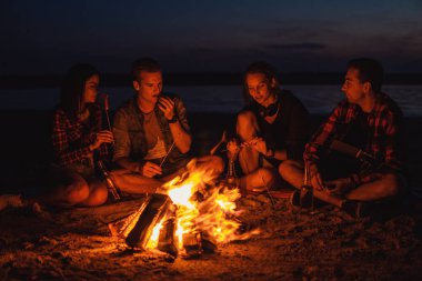 Sahilde kamp. Grup Genç arkadaşlar şenlik ateşi ile piknik. Onlar ateşten sosis yemek