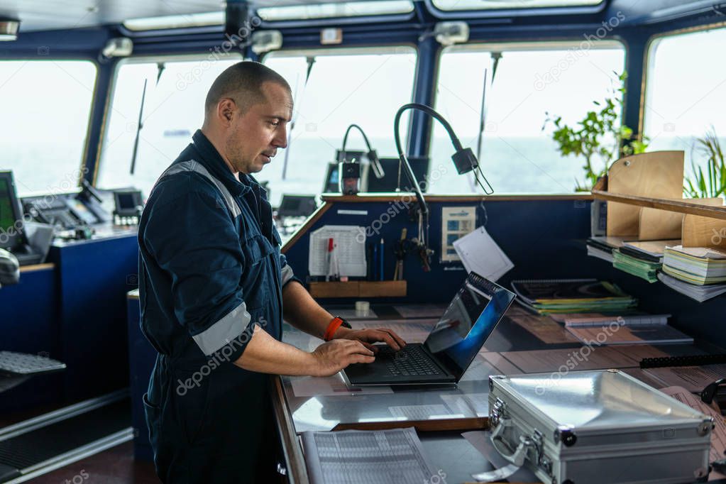 Marine navigational officer is using laptop or notebook at sea