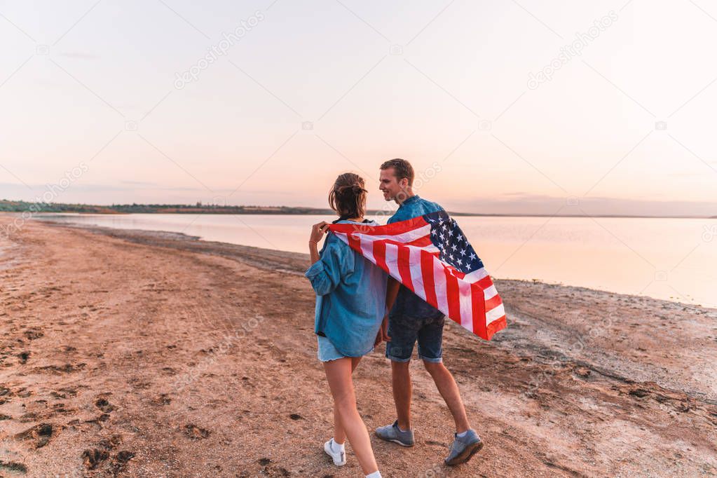 american couple covered in american flag walking on beach
