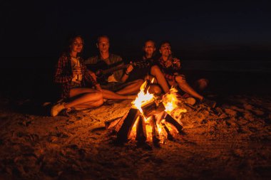 Sahilde kamp. Grup Genç arkadaşlar şenlik ateşi ile piknik. Adam gitar çalıyor