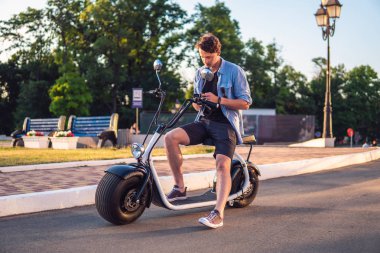 Elektrikli bisiklet veya scooter üzerinde oturan yakışıklı genç adam