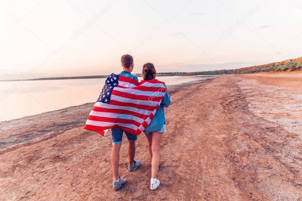 american couple covered in american flag walking on beach