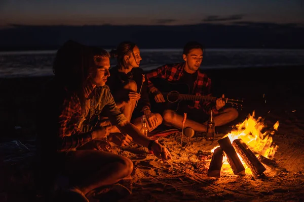 Jóvenes amigos tienen picnic con hoguera en la playa — Foto de Stock