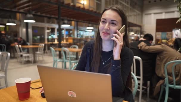 Молодая, красивая девушка работает с ноутбуком и пьет кофе за деревянным столом — стоковое видео
