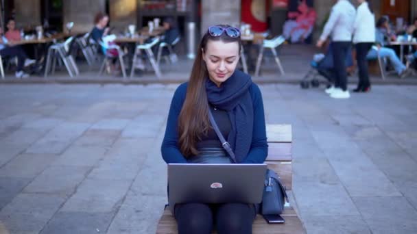 Κομψό νεαρή γυναίκα που κάθεται με ένα laptop σε εξωτερικούς χώρους σε πλατεία της πόλης — Αρχείο Βίντεο