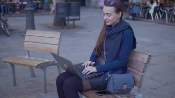 Элегантная молодая женщина сидит с ноутбуком на улице на городской площади — стоковое видео