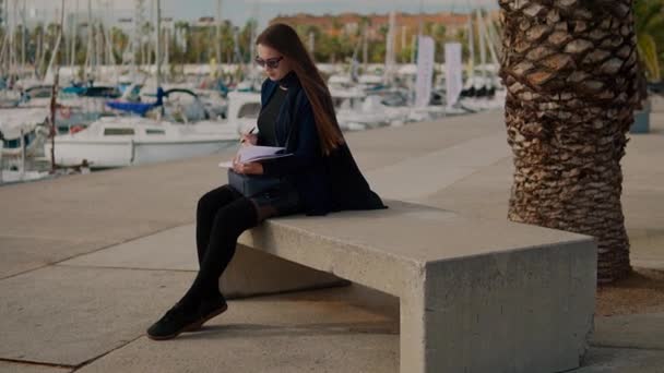 Mujer dibujando bocetos en su cuaderno al aire libre. Palmeras y yates sobre fondo — Vídeos de Stock