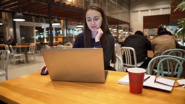 Νεαρό, όμορφο κορίτσι με φορητό υπολογιστή και πίνοντας τον καφέ σε ένα ξύλινο τραπέζι — Αρχείο Βίντεο