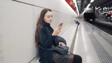 Smartphone cep telefonu ile metro istasyonunda tipik bir kadın. Tren bekliyor