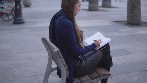 Mujer dibujando bocetos en su cuaderno de bocetos al aire libre sentado en la plaza de la ciudad — Vídeos de Stock