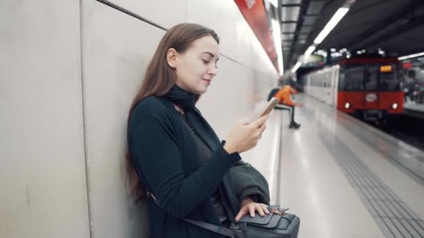 Mujer escribiendo en el teléfono inteligente en la estación de metro. Esperando el tren — Vídeos de Stock