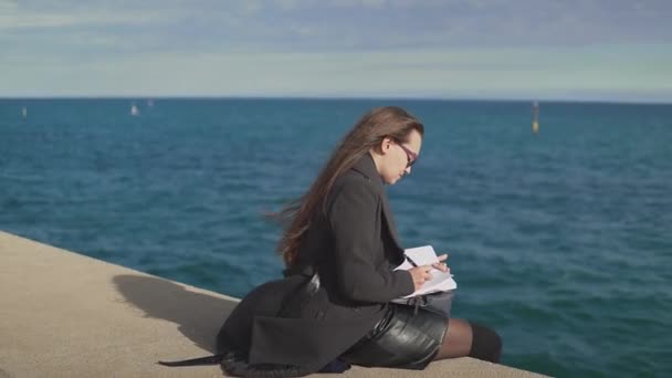 Mujer dibujando bocetos en su cuaderno al aire libre cerca del mar — Vídeo de stock