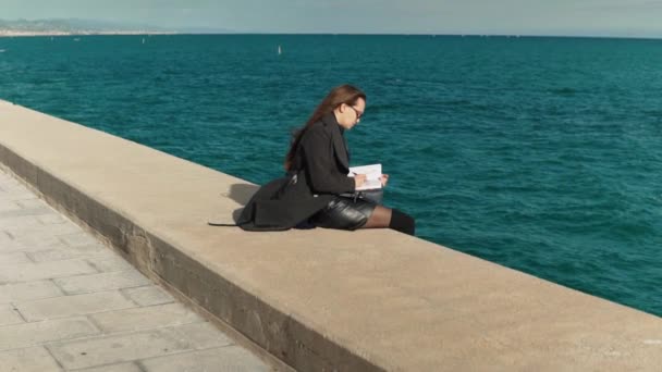 Wanita menggambar sketsa di buku sketsanya di luar ruangan dekat laut. slowmotion shot — Stok Video