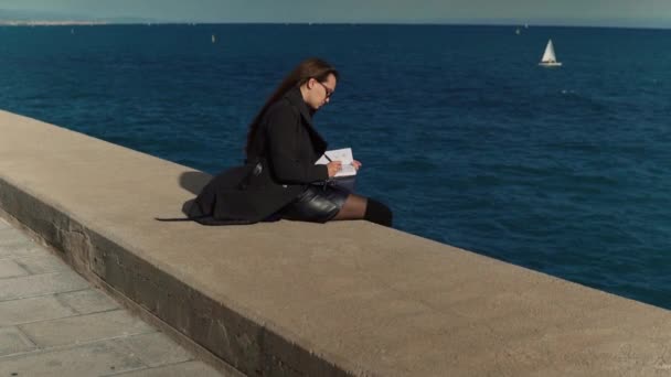 Mujer dibujando bocetos en su cuaderno de bocetos al aire libre cerca del mar. disparo en cámara lenta — Vídeo de stock