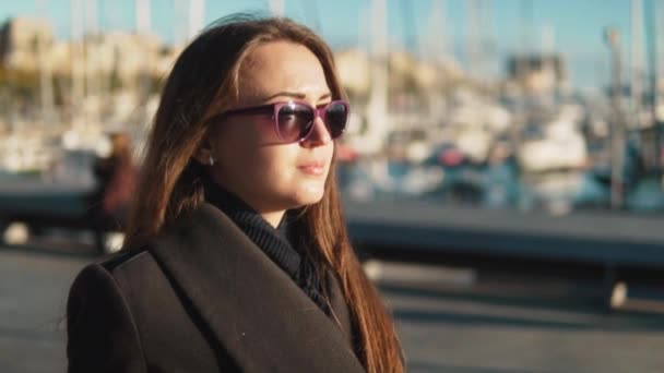 Женщина в солнцезащитных очках идет с большим количеством яхт и лодок позади — стоковое видео