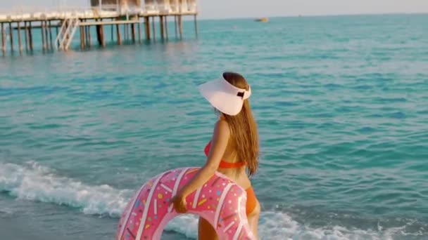Jeune femme flottant avec un beignet gonflable, face arrière — Video
