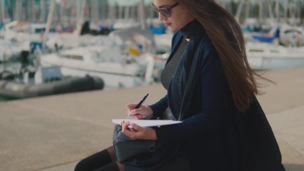 Frau zeichnet Skizzen in ihrem Skizzenbuch outdoor. Yachten im Hintergrund — Stockvideo