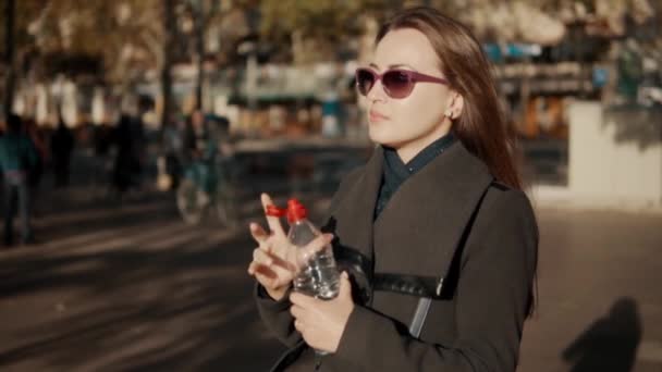 Sedienta mujer de negocios abriendo botella y bebiendo agua al aire libre — Vídeo de stock