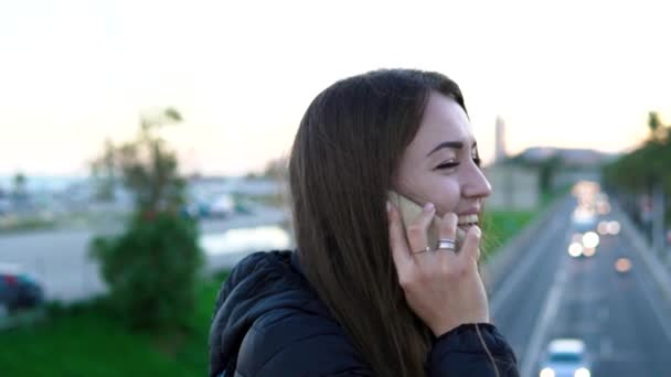 Jonge mooie vrouw praten over de telefoon op een brug van de stad — Stockvideo