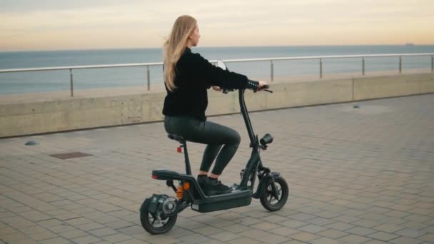 Mooie blonde vrouw rijden elektrische fiets in de buurt van de zee. — Stockvideo