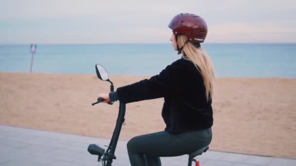 Ładna Blondynka kobieta jazdy rower elektryczny, w pobliżu morza. — Wideo stockowe