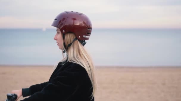 Гарненька білявка жінка за кермом електричний велосипед біля моря . — стокове відео