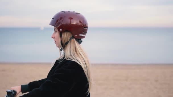 Mujer rubia bonita conduciendo bicicleta eléctrica cerca del mar . — Vídeos de Stock