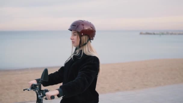 Mooie blonde vrouw rijden elektrische fiets in de buurt van de zee. — Stockvideo