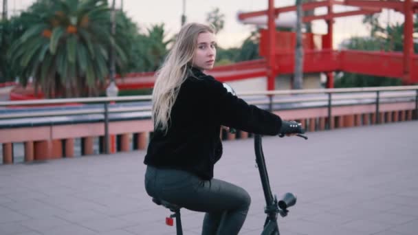 Mulher loira bonita dirigindo bicicleta elétrica na cidade — Vídeo de Stock