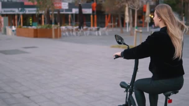 Mulher loira bonita dirigindo bicicleta elétrica na cidade — Vídeo de Stock