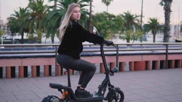 Mulher loira bonita dirigindo bicicleta elétrica na cidade — Vídeo de Stock