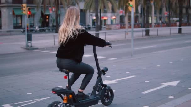 Mujer rubia bonita conduciendo bicicleta eléctrica en la ciudad — Vídeos de Stock