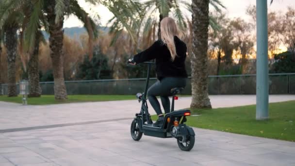 Mulher loira bonita dirigindo bicicleta elétrica no parque da cidade — Vídeo de Stock