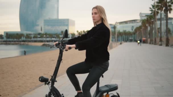 Mooie blonde vrouw rijden elektrische fiets in de buurt van de zee — Stockvideo