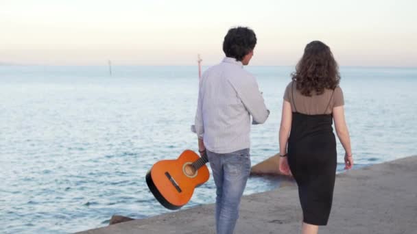 Hermosa pareja de músicos a pie a lo largo del muelle junto al mar — Vídeos de Stock