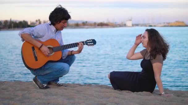 Bela casal músico sentado ao longo do cais junto ao mar — Vídeo de Stock