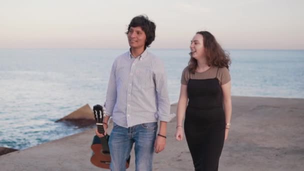 Bela caminhada casal músico ao longo do cais junto ao mar — Vídeo de Stock