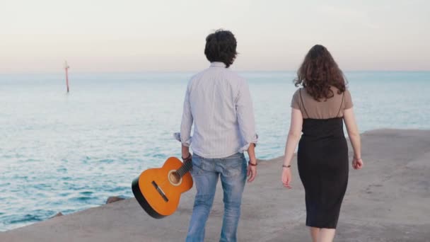 Bela caminhada casal músico ao longo do cais junto ao mar — Vídeo de Stock