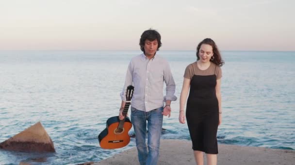 Hermosa pareja de músicos a pie a lo largo del muelle junto al mar — Vídeos de Stock