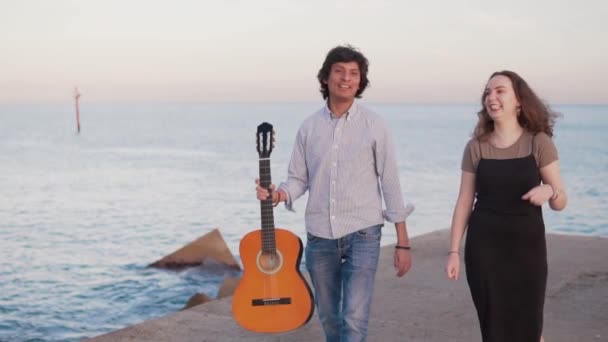 Bela caminhada casal músico ao longo do cais junto ao mar — Vídeo de Stock