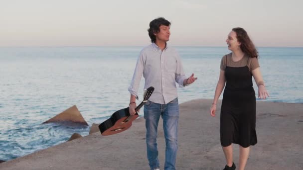 Bela caminhada casal músico ao longo do cais junto ao mar — Vídeo de Stock