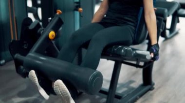Genç kadının bacak yapması uygun eğitim makinasıyla spor salonunda egzersiz. İleri gelen görüntüleyin. 4k vurdu