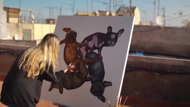 Молода жінка малює художника на даху будинку — стокове відео