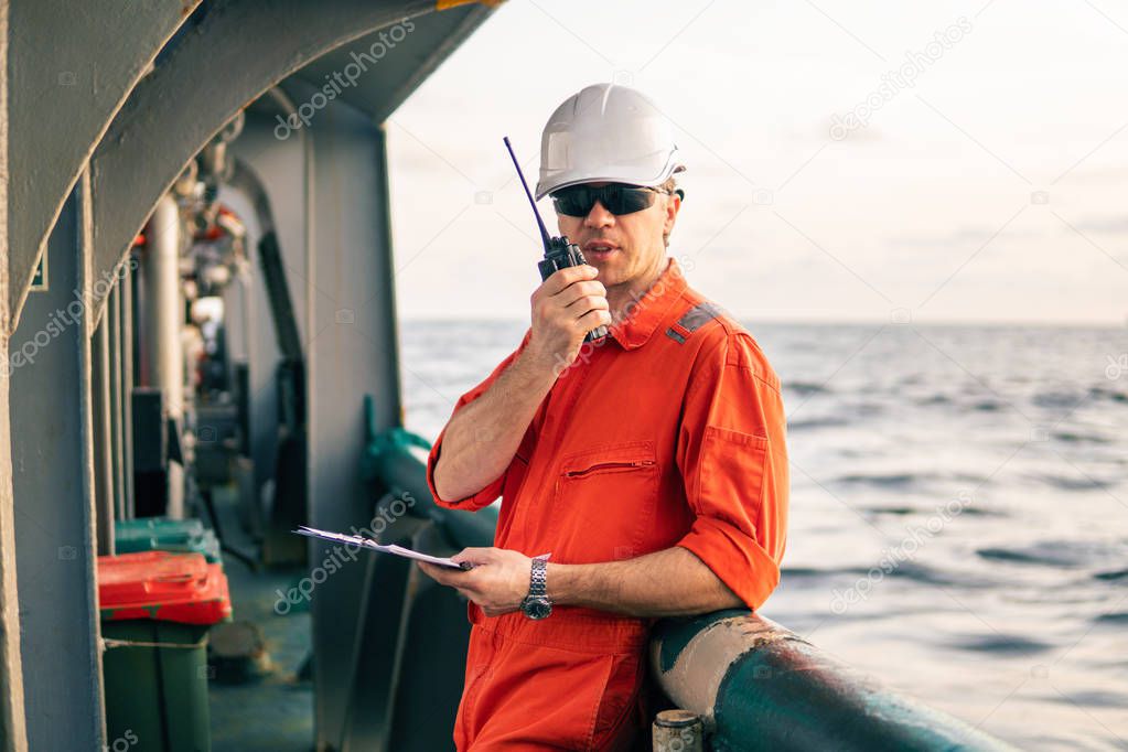 Deck Officer on deck of offshore vessel holds VHF walkie-talkie radio