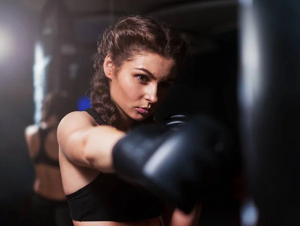 Young fighter boxer girl in training with heavy punching bag