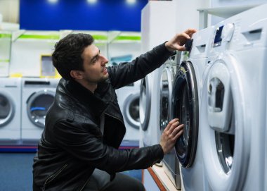 erkek müşteri süpermarkette çamaşır makinesi seçimi.