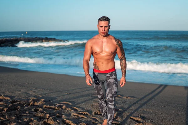 Tattooed bodybuilder sexy male coach at the beach.