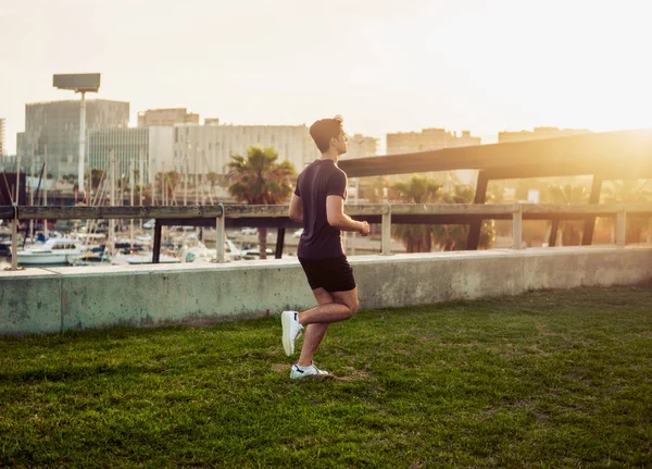 Hombre atlético joven corriendo en el parque con antecedentes de rascacielos —  Fotos de Stock